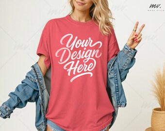 May include: A coral-colored t-shirt with the text "Your Design Here" in a white script. The model is wearing a light blue denim jacket. The image is a product mockup, ideal for showcasing custom designs on apparel.