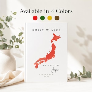 May include: A white journal featuring the text "EMILY WILSON" and a red watercolour map of Japan. The cover also includes the text "MY TRIP TO Japan" and "SEPTEMBER 2024". The top of the journal reads "Available in 4 Colors" with colour swatches.