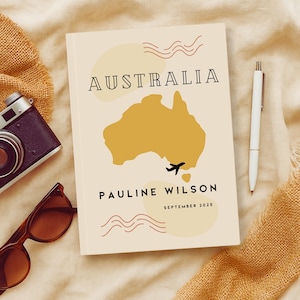 Puede incluir: Un cuaderno de color crema con un mapa de Australia, un icono de avión y el texto "AUSTRALIA", "PAULINE WILSON" y "SEPTEMBER 2025".