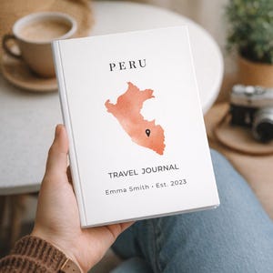 Könnte beinhalten: Ein weißes Reisetagebuch mit dem Wort "PERU" oben und einer orangefarbenen Aquarellkarte von Peru. Der Text "TRAVEL JOURNAL" und "Emma Smith • Est. 2023" sind darunter gedruckt. Das Tagebuch wird in einer Hand gehalten.