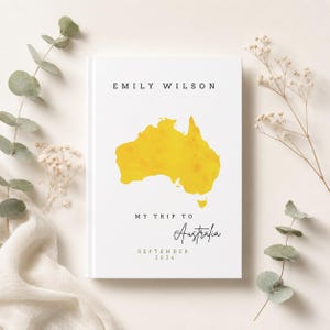 Könnte beinhalten: Ein weißes Notizbuch mit dem Text "Emily Wilson" oben und einer gelben Karte von Australien. Darunter steht "My Trip to Australia" und "September 2024".