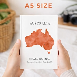Puede incluir: Diario de viaje tamaño A5 con la palabra "AUSTRALIA" sobre un mapa naranja de Australia. Las palabras "TRAVEL JOURNAL" y "Emma Smith • Est. 2023" están impresas debajo en la portada blanca.