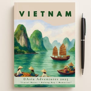 May include: A notebook featuring a watercolour illustration of Halong Bay, Vietnam. The cover displays the text "VIETNAM" and "Asia Adventures 2025". A black pen is positioned to the right of the notebook.