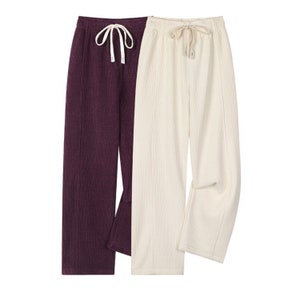 May include: Two pairs of wide-leg trousers. One is a deep burgundy, the other off-white. Both have a ribbed texture, drawstring waistbands, and a split hem. A casual, comfortable style.