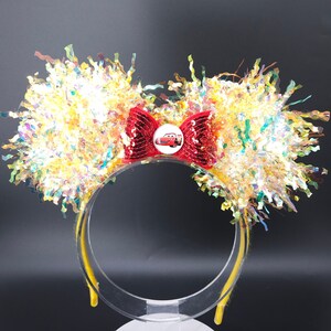 Puede incluir: Diadema de orejas de Minnie Mouse amarilla e iridiscente con un lazo rojo y un botón de coche rojo con Rayo McQueen de la película Cars de Disney Pixar.