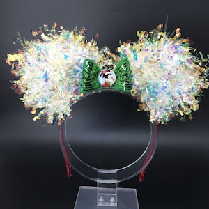 Può includere: Fascetta festiva con grandi orecchie soffici in orpello iridescente multicolore. Un fiocco verde con paillettes presenta una grafica di Topolino. La fascia rossa e trasparente è perfetta per una festa o una visita al parco a tema Disney.