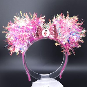 Könnte beinhalten: Ein rosa Stirnband mit flauschigen rosa Ohren und einer glitzernden rosa Schleife mit einer Figur aus dem Film Inside Out.