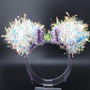 May include: Purple headband with iridescent glitter ears and a purple bow with a green button featuring a cartoon character.