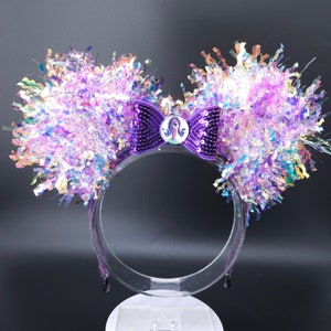 May include: Purple and iridescent Minnie Mouse ears with a purple sequin bow and a character from the film Inside Out in the centre of the bow.