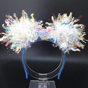 Może przedstawiać: Niebieska opaska do włosów z dużymi, puszystymi, białymi i opalizującymi akcentami. Opaska posiada cekinową sylwetkę Myszki Miki pośrodku. Akcenty wykonane są z lamety i wstążki.