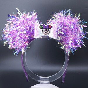 Puede incluir: Diadema de orejas de Minnie Mouse de color morado e iridiscente con un lazo blanco y una cara de Minnie Mouse del Día de los Muertos en el lazo.