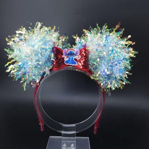 Può includere: Una fascia festiva con grandi orecchie soffici in orpello iridescente. La fascia rossa presenta un fiocco di paillettes con un design del personaggio Stitch. Le orecchie sono un mix di orpello blu, argento e verde, creando un effetto scintillante.
