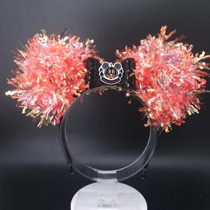 May include: Halloween-themed headband with large, fluffy, red and gold tinsel ears. A black bow with a pumpkin and the words "Trick or Treat" is centered on the headband. The ears are attached to a clear plastic headband.