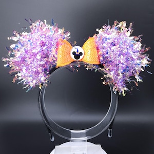 May include: Purple and iridescent Minnie Mouse ears with an orange bow and a black and white Mickey Mouse head with a witch's hat on top.