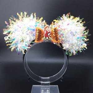 May include: A pair of black mouse ears with iridescent white and gold pom-poms. A gold sequin bow with a cartoon image of Doc from Snow White and the Seven Dwarfs is in the center.