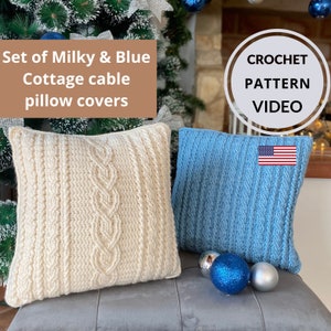 May include: Two crocheted pillow covers, one white and one blue, with a cable knit pattern. The pillows are on a gray couch with blue and silver ornaments. The text "CROCHET PATTERN VIDEO" is in a circle above the pillows.