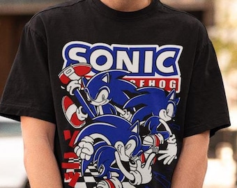 May include: A black t-shirt with a graphic print of Sonic the Hedgehog. The graphic features Sonic and two other characters from the video game series. The text "SONIC THE HOG" is printed above the characters.