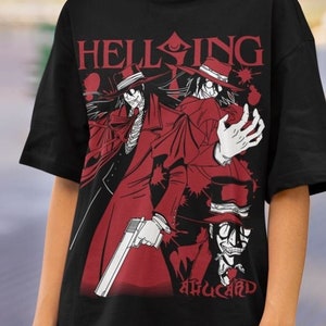 Puede incluir: Camiseta negra con un gráfico rojo de personajes de anime y la palabra "HELLSING". El diseño incluye un personaje con sombrero y pistola. La camiseta es de cuello redondo.