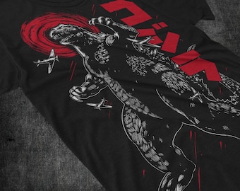 May include: Black t-shirt with a white graphic of Godzilla destroying fighter jets. The graphic includes the Japanese word "Gojira" in red.