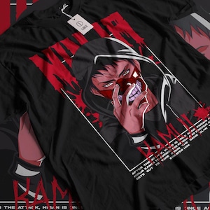 May include: Black t-shirt with a red and white graphic of a masked character. The text "After the attack, Hitan is inle a ain known a ninja kamui too avengit his family and friends a sets out to take down the same clan created him. Is once a" is printed on the shirt.
