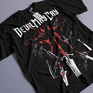 Peut inclure: T-shirt noir avec un motif blanc d'un personnage du jeu vidéo Devil May Cry. Le personnage tient une épée et est entouré d'autres épées. Le texte "Devil May Cry" est écrit en lettres blanches au-dessus du personnage.