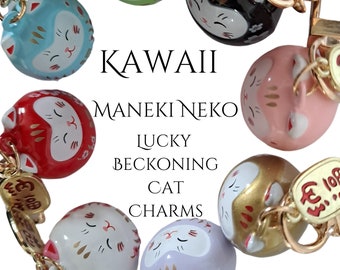 May include: A selection of Kawaii Maneki Neko Lucky Beckoning Cat charms in a variety of colours, such as red, green, black, pink, gold, blue, white, and purple. Each charm features a gold-coloured keychain and a small tag with Japanese characters.