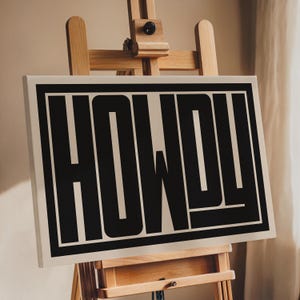 May include: A beige canvas print with a black border and the word "HOWDY" in bold black letters.