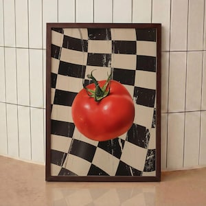 May include: A framed print showing a ripe red tomato with green stems, set against a black and white chequered flag design. The frame is dark brown. The artwork is a food-themed decorative piece.
