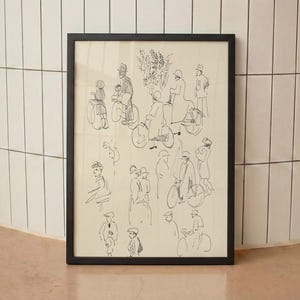 May include: A framed wall art print featuring a black ink line drawing on a cream background. The illustration depicts a busy street scene with multiple figures, some riding bicycles and others standing, rendered in a loose, minimalist sketch style.
