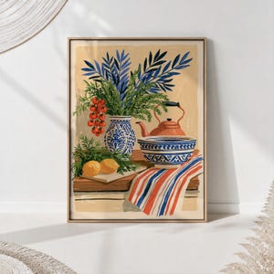 Op de afbeelding: Een ingelijste kunstdruk met een stilleven van een blauw-witte vaas met blauw gebladerte, een tros rode cherrytomaatjes, twee gele citroenen, een terracotta theepot, een blauw-witte kom en een gestreepte doek op een tafel.