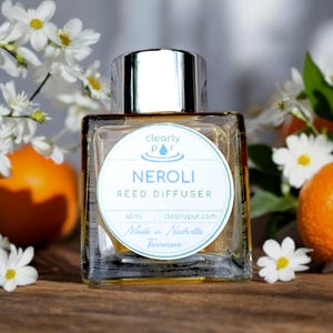 May include: A clear glass bottle with a silver lid and a white label that reads "clearly pur" and "NEROLI REED DIFFUSER". The label also includes the text "60ml", "clearlypur.com", and "Made in Nashville Tennessee".