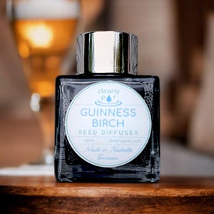 May include: A dark blue glass bottle with a silver lid and a white label that reads "clearly pur" and "GUINNESS BIRCH REED DIFFUSER 60ml clearlypur.com Made in Nashville Tennessee".