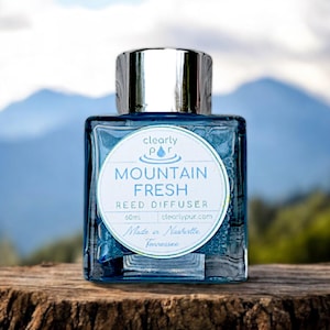May include: A clear glass bottle with a silver lid and a white label that reads "clearly pur" with a water drop logo. The label also reads "Mountain Fresh Reed Diffuser 60ml clearlypur.com Made in Nashville Tennessee".