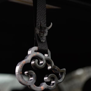 Può includere: Un ciondolo per auto in pelle nera con un pendente a forma di nuvola argentata e un piccolo ciondolo a forma di testa di demone.
