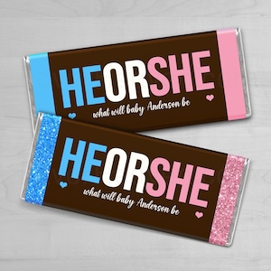 May include: Two chocolate bars with the text "HE OR SHE" in blue and pink, with the words "what will baby Anderson be" below. One bar has blue glitter, the other pink glitter.