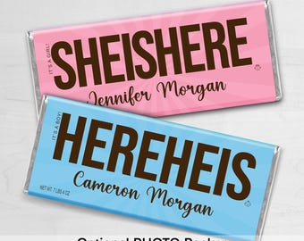 May include: Two candy bars, one pink and one blue, with brown text. The pink bar reads "SHEISHERE" and "Jennifer Morgan." The blue bar reads "HEREHEIS" and "Cameron Morgan." The bars are wrapped in silver foil.