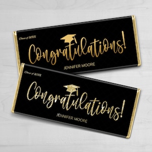 May include: Two black chocolate bar wrappers with gold foil accents. The wrappers feature a gold graduation cap and the text "Congratulations!" with the name "Jennifer Moore" and "Class of 20XX".