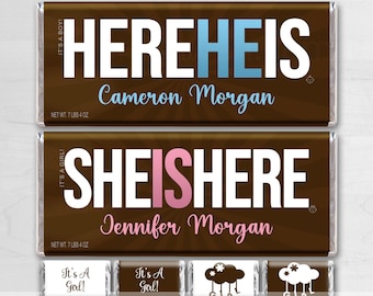 May include: Two chocolate bar wrappers with the text "HERE HE IS" and "SHE IS HERE" in white with blue and pink accents. The wrappers are brown with a swirl pattern. The text "Cameron Morgan" and "Jennifer Morgan" are printed below the main text. The wrappers are for a baby shower.