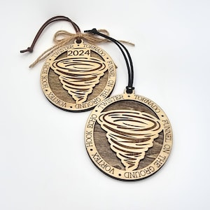 May include: Two wooden ornaments shaped like a tornado with the words "Hook Echo", "Vortex", "Twister", "Tornado", "Funnel on the Ground" and "2024" engraved on them.