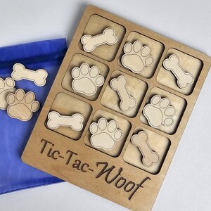 May include: A wooden tic-tac-toe game with a paw print and bone design. The game is called "Tic-Tac-Woof" and comes with a blue drawstring bag containing extra pieces.