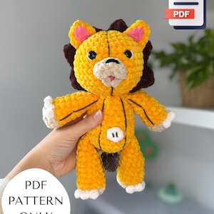 Puede incluir: Un león de ganchillo amarillo hecho a mano con una melena marrón, patas blancas y un hocico beige. El león tiene ojos negros y boca rosa. La imagen incluye un icono PDF y el texto "PDF PATTERN ONLY".