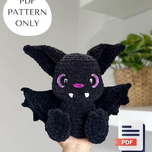Puede incluir: Un peluche de murciélago negro tejido a ganchillo con grandes ojos morados brillantes y una boca rosa. El murciélago tiene colmillos blancos y alas extendidas. La imagen incluye el texto "PDF PATTERN ONLY" y un icono PDF.
