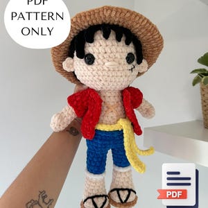 Puede incluir: Muñeco de ganchillo hecho a mano de un personaje con sombrero de paja, chaleco rojo, pantalones azules y faja amarilla. El muñeco tiene pelo negro y una pequeña cicatriz debajo del ojo izquierdo. Incluye el texto "PDF PATTERN ONLY".