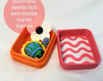 May include: A rectangular orange container and a separate pink lid with a wavy pattern, containing a small blue and green beetle figurine, a white flower-shaped object with a black center, and a tiny purple component. Text reads SURPRISE Beetle Box with Beetle Purse Games.