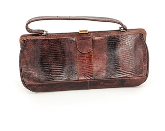 Peut inclure: Une pochette en cuir marron avec un motif de peau de serpent texturé. La pochette a un fermoir doré et une seule sangle.