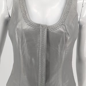 May include: A silver leather vest with a braided trim around the neckline and down the front. The vest has a scoop neckline and a cropped length.