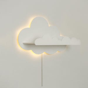 May include: White cloud-shaped shelf with a built-in light. The shelf is mounted on a white wall and has a cord hanging down.