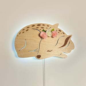 May include: A wooden deer night light with a light blue glow and pink flowers on its head.