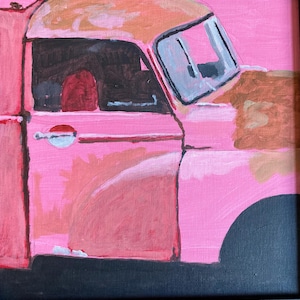 May include: A pink painting of a vintage pickup truck. The truck's body is a vibrant pink, with areas of rust-coloured paint. The windows are outlined in grey, and the tyres are black. The painting is framed in a black square.