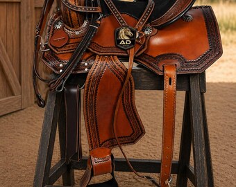 May include: A brown leather saddle with intricate tooling and decorative silver-tone accents. The saddle features a black seat and is displayed on a wooden stand. The saddle has the letters "AD" and a horse head logo.